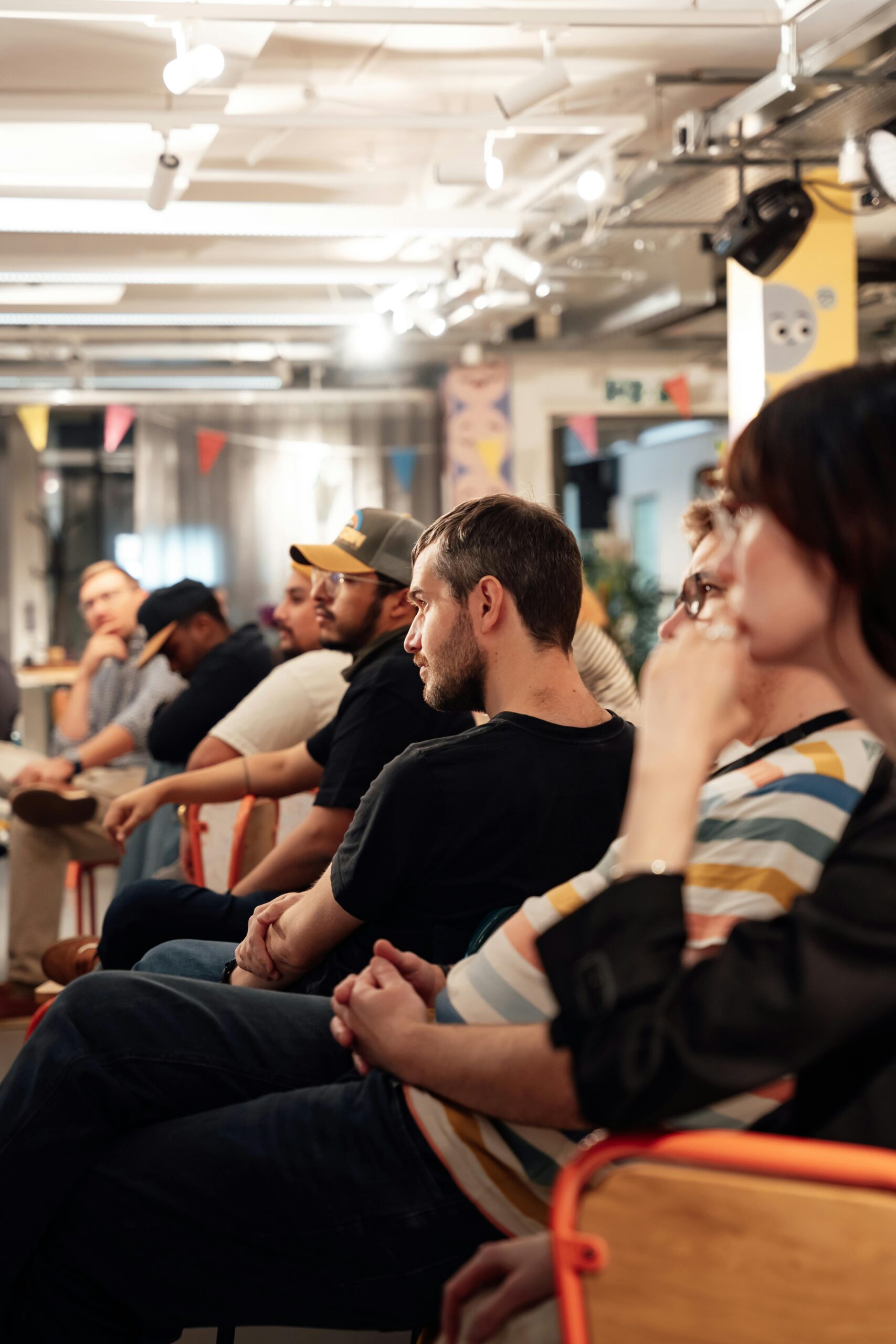 A group of diverse adults attentively listening in a casual indoor event setting.